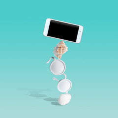 Creative composition with seashells, white sunglasses and smartphone on pastel blue background. Summer minimal concept.