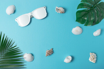 Creative composition with seashells, white sunglasses and palm leaves on pastel blue background. Summer minimal concept.