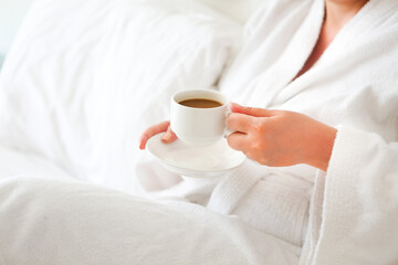 Woman wearing white robe with cup of coffee in her hands