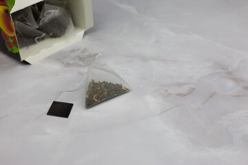 Pyramid shaped tea bag with a string and a hand holder rests on a white marble table next to an open package