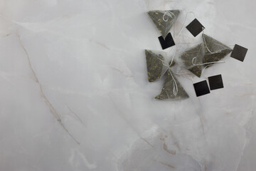 Tea bags in the shape of pyramids with tea leaves with fruity flavor lie on a white marble table