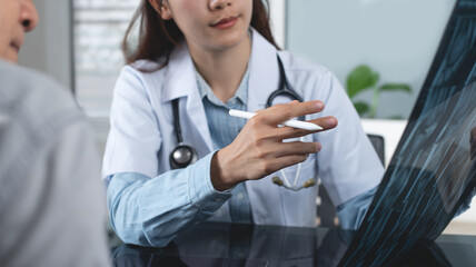 Female asian orthopedic doctor showing MRI bone scan to patient, explaining checkup result, medical...