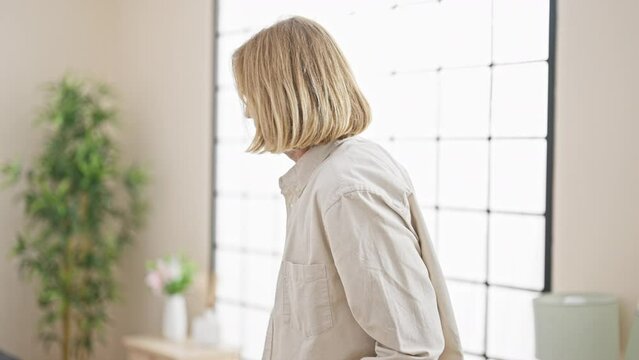Injured man with long blond hair limps using crutches in a modern bedroom, showing pain and discomfort.
