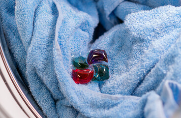 Laundry detergent capsule in washing machine drum on a blue towel, close-up view