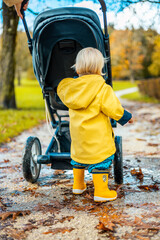 Sun always shines after the rain. Small blond infant boy wearing yellow rubber boots and yellow...