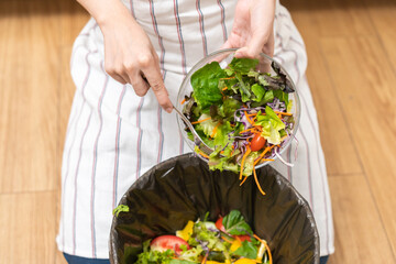 Compost from leftover food asian young housekeeper woman, female hand holding salad bowl use fork scraping waste, rotten vegetable throwing away into garbage, trash or bin. Environmentally responsible