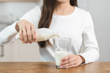Health care, asian young woman, girl hand pouring of fresh, dairy milk from bottle into glass, drinking and eating breakfast in morning at kitchen home. Calcium, protein for healthy lifestyle people