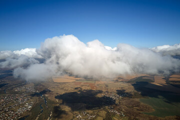 Aerial view from airplane window at high altitude of distant city covered with puffy cumulus clouds forming before rainstorm