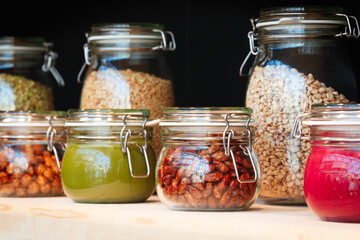 Glass jars with grain, nuts, butter, jam on the wooden shelf  on background of a dark wall, breakfast concept, kitchen background, healthy eating concept, conservation concept