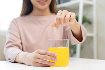 Close up young woman hand holding glass of water after putting or dropping yellow effervescent...