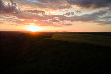 Bright colorful sunset sky with setting sun and vibrant clouds over dark landscape
