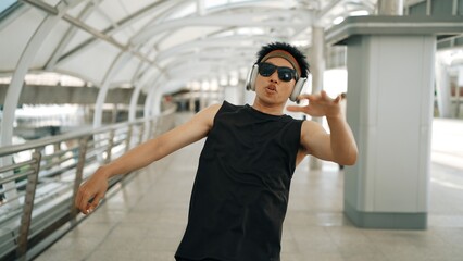 Fototapeta premium Closeup of smart handsome dancer moving hands while dance to hip hop music. Asian hipster wearing headphone while walking along the corridor with blurring background. Outdoor sport 2024. Sprightly.