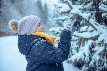 happy girl actively plays outside during the day. in winter looking at the snow on a spruce branch