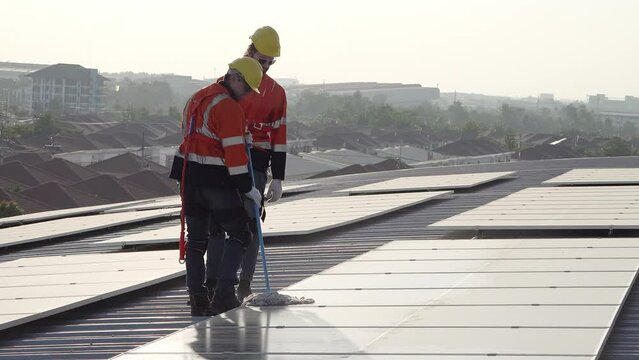 A technician sits on a rooftop, examining solar panels under a clear blue sky. He points while taking notes, ensuring everything is functioning properly.