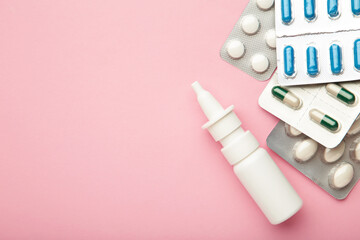 Nasal spray with pills on pink background. Top view