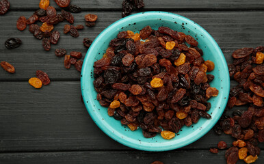 Raisins in blue plate on black wooden background.