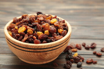 Dry raisins in wooden bowl on brown wooden background.
