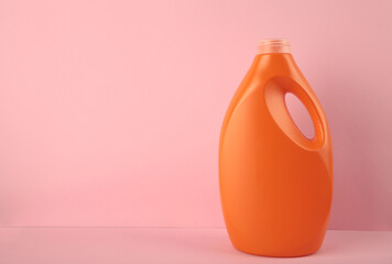 Orange plastic bottle with liquid laundry detergent or cleaning agent or bleach or fabric softener on pink background.