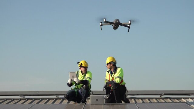 A technician sits on a rooftop, examining solar panels under a clear blue sky. He points while taking notes, ensuring everything is functioning properly.
