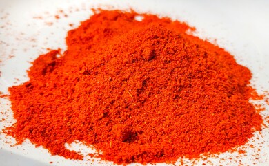 Organic Indian red chilly or chilli pepper spice powder heap or pile scatter and isolated on white background. Closeup macro top side view. Spicy paprika, mirchi and chilli hot food flavouring powder.
