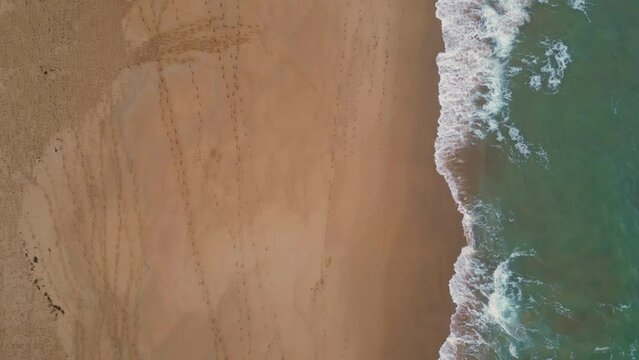 Aerial scenic ocean water washing golden sand on empty beach. Waves splashing