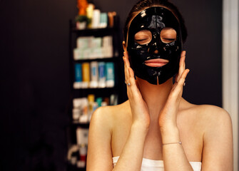 Beautiful caucasian woman with black silicone mask for the skin. Pretty brunette female with cosmetic mask on her face.