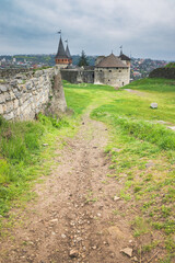 Fototapeta na wymiar Old Kamianets-Podilskyi Castle under a cloudy grey sky. The fortress located among the picturesque nature in the historic city of Kamianets-Podilskyi, Ukraine