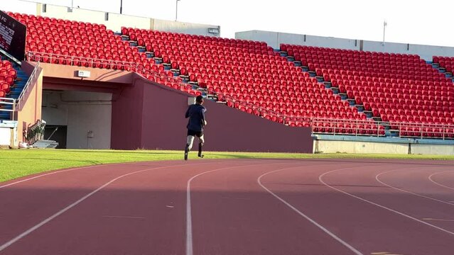 Asian para-athlete with prosthetic blades leg in stadium practicing workout for Paralympic running competition. Amputee sportsman runner practicing running workout. Disabled athlete man sport concept.