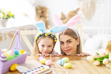 Obraz na płótnie Canvas easter, mom and little daughter with bunny ears on their head are preparing for the holiday by having fun playing and spending time together, colorful eggs, lifestyle,