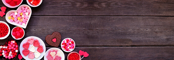 Valentines Day candy corner border with an assortment of sweets. Above view on a dark wood banner background with copy space.