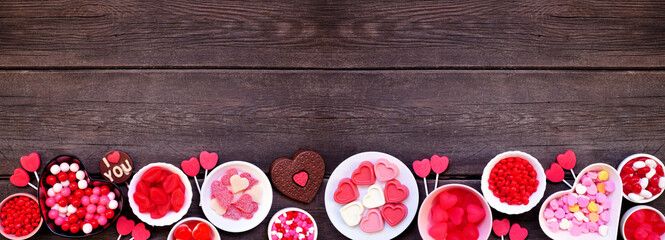 Valentines Day candy bottom border with assorted sweets. Above view on a dark wood banner...