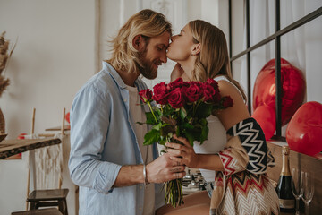 Young loving couple embracing and kissing while woman holding flower bouquet at the decorated home
