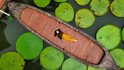 Asian woman relaxing on a long tail boat surrounded by giant Victoria Waterlillies in tropical rainforest at Phuket Thailand