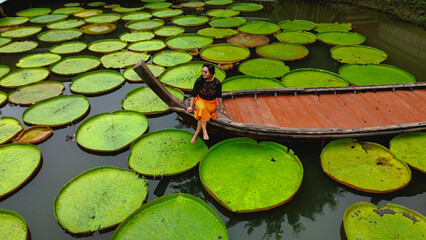 Drone shot of Girl on Boat surrounded by Victoria Amazonica Natural landscape aquatic plants - obrazy, fototapety, plakaty
