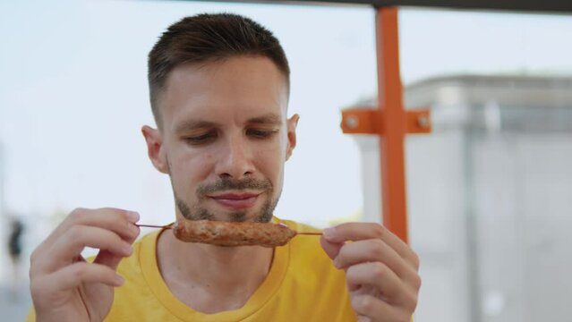 Portrait of man enjoying smell of grilled minced meat on skewer on terrace at local cafe. Appetizing traditional Balkan sausages cevapi made from baked ground meat with onions and seasonings.