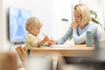 Caring young Caucasian mother and small son drawing painting in notebook at home together. Loving...