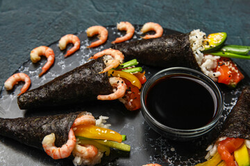 Board with tasty sushi cones, shrimps and soy sauce on dark color background, closeup