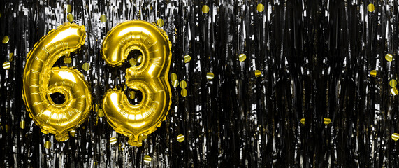 Gold foil balloon number number 63 on a background of black tinsel decoration. Birthday greeting...