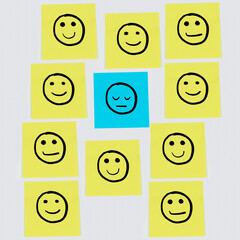 Smiley faces drawn on yellow post-its surrounding a sad face drawn on a blue pot-it with a white background