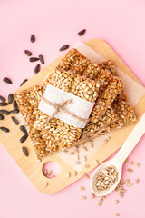 Board with tasty kozinaki and sunflower seeds on pink background