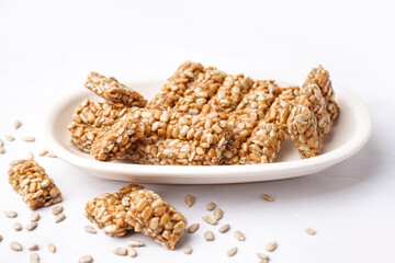 Plate with tasty pieces of kozinaki and sunflower seeds on white background