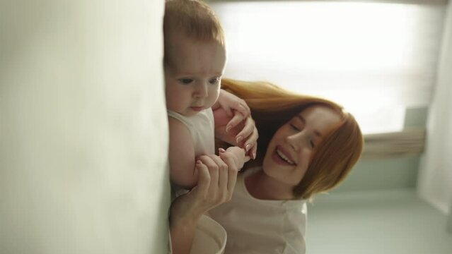 Close up shot of young neo mother is playing with newborn baby, touches his little chubby arms. Innocence and wonder of motherhood and childhood. Cinematic advertisement, baby care, vertical video