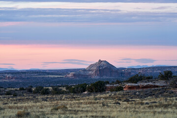 A large rock mountain stands out of the surrounding landscape and grassland, beautifully set against a colorful pink and purple sunset.