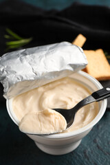 Plastic container with tasty cream cheese on black background