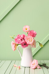 Jug with beautiful pink eustoma flowers on green wooden table