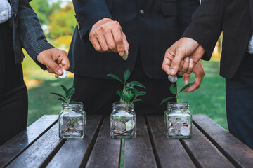 Business people put coin to money saving glass jar on outdoor table as sustainable money growth investment or eco-subsidize. Green corporate promot and invest in environmental awareness. Gyre - obrazy, fototapety, plakaty