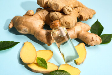 Bottle of ginger cosmetic oil and leaves on blue background