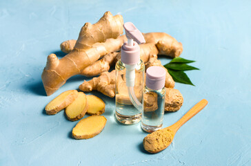 Bottles of ginger cosmetic oil and wooden spoon with dried powder on blue background