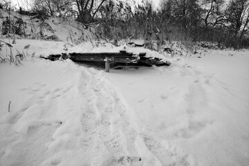 Frozen lake in the winter. Broken wooden handmade footbridge frozen in ice. Black and white photo.