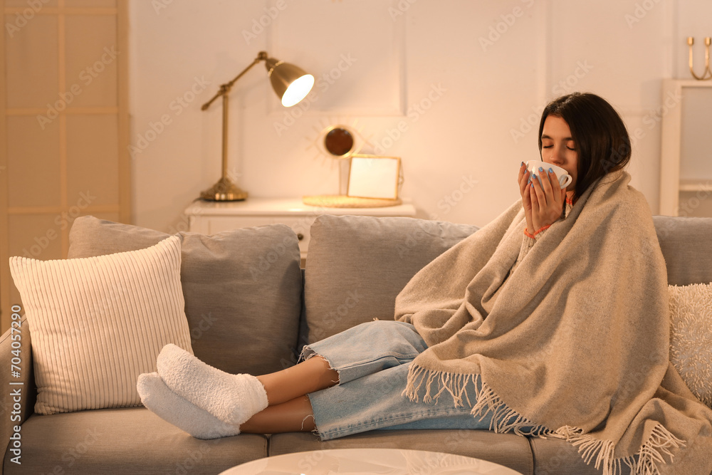 Poster Young woman with plaid and cup of hot coffee at home in evening